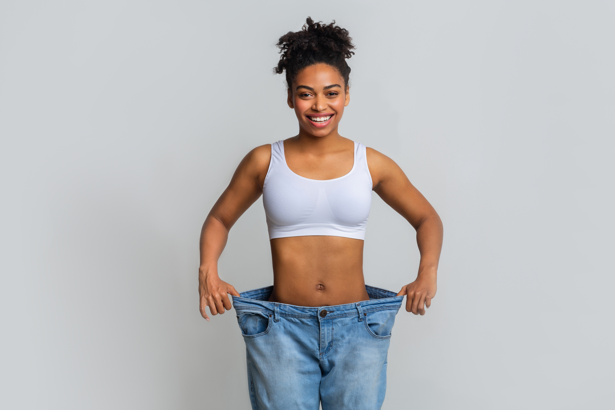 Happy young woman with too large jeans Woman experiencing success with semaglutide weight loss program Next Level Wellness in Illinois and the greater Chicago area